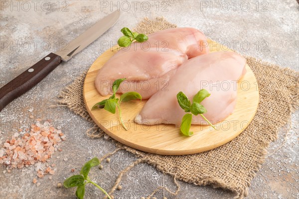 Raw chicken breast with herbs and spices on a wooden cutting board on a brown concrete background. Side view, close up