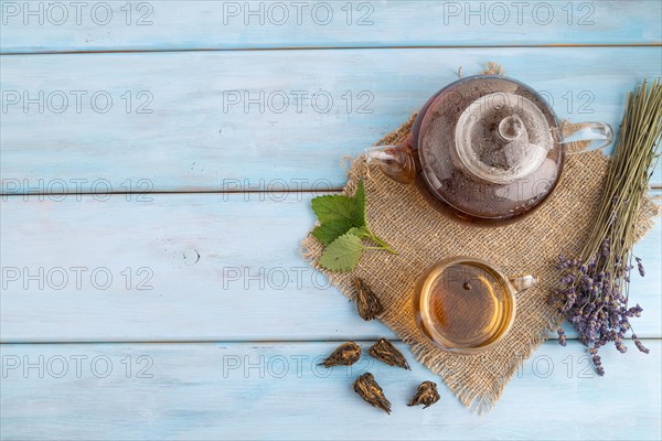 Red tea with herbs in glass on blue wooden background and linen textile. Healthy drink concept. Top view, flat lay, copy space