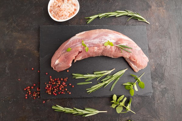 Raw pork meat with herbs and spices on slate cutting board on black concrete background. Top view, flat lay, close up