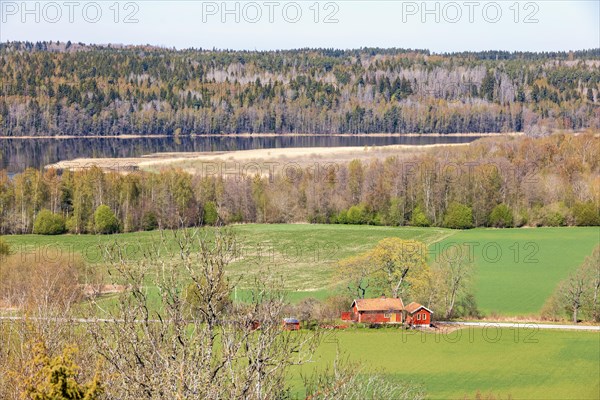 High angle view at a red house on a field in the swedish countryside with a lake and forest at springtime, Sweden, Europe