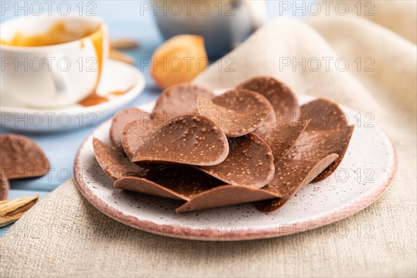 Chocolate chips with cup of coffee and caramel on a blue wooden background and linen textile. side view, close up, selective focus