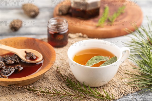 Pine cone jam with herbal tea on gray wooden background and linen textile. Side view, close up, selective focus