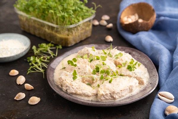 Stewed chicken fillets with coconut milk sauce and rucola microgreen on black concrete background and blue linen textile. side view, close up, selective focus