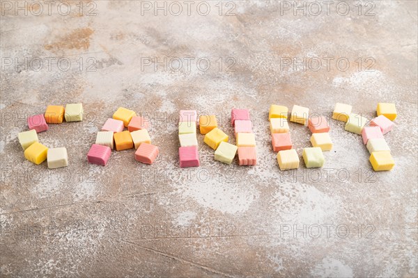 The inscription candy laid out with various fruit jelly chewing candies on brown concrete background. apple, banana, tangerine, side view, copy space