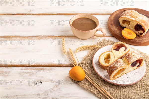 Homemade sweet bun with apricot jam and cup of coffee on white wooden background and linen textile. side view, copy space