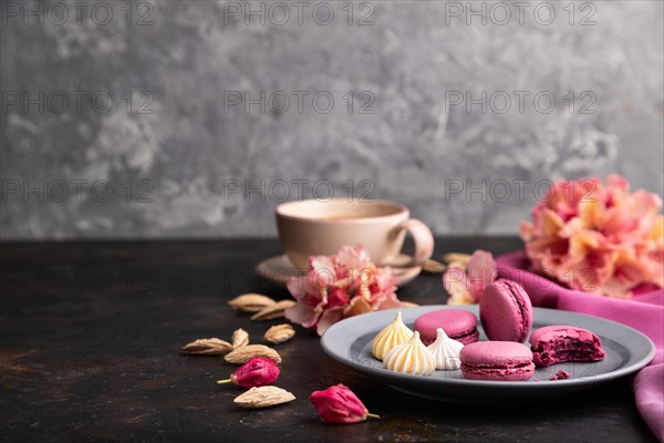 Purple macarons or macaroons cakes with cup of coffee on a black concrete background and pink textile. Side view, copy space, selective focus