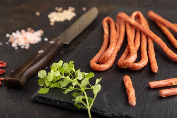 Traditional polish smoked pork sausage kabanos on a slate cutting board with salt and pepper on black concrete background. Side view, close up, selective focus