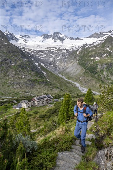 Two mountaineers on a hiking trail in a picturesque mountain landscape with alpine roses, in the background mountain peak Grosser Moeseler with glacier Waxeggkees and mountain hut Berliner Huette, Berliner Hoehenweg, Zillertal Alps, Tyrol, Austria, Europe