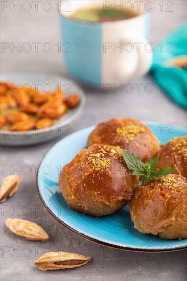 Homemade traditional turkish dessert sekerpare with almonds and honey, cup of green tea on gray concrete background and blue textile. side view, selective focus