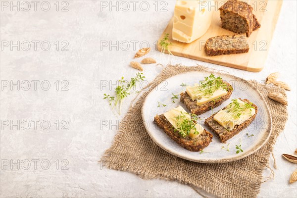 Grain bread sandwiches with cheese and watercress microgreen on gray concrete background and linen textile. side view, copy space
