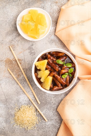 Tteokbokki or Topokki, fried rice cake stick, popular Korean street food with spicy jjajang sauce and pineapple on gray concrete background and orange textile. Top view, flat lay