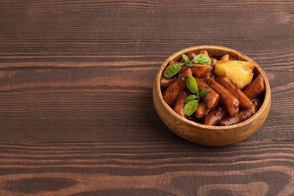 Tteokbokki or Topokki, fried rice cake stick, popular Korean street food with spicy jjajang sauce and pineapple on brown wooden background. Side view, copy space