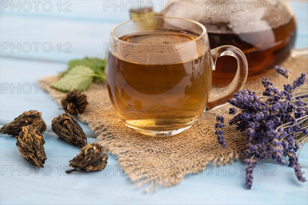 Red tea with herbs in glass on blue wooden background and linen textile. Healthy drink concept. Side view, close up, selective focus