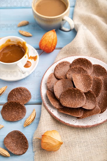 Chocolate chips with cup of coffee and caramel on a blue wooden background and linen textile. side view, close up, selective focus