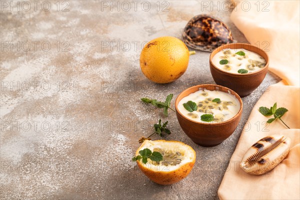 Yoghurt with granadilla and mint in clay bowl on brown concrete background and orange linen textile. side view, copy space