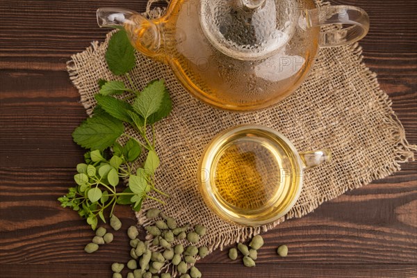 Green oolong tea with herbs in glass on brown wooden background and linen textile. Healthy drink concept. Top view, flat lay