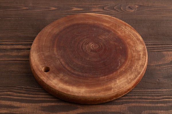 Empty round wooden cutting board on brown wooden background. Side view, close up