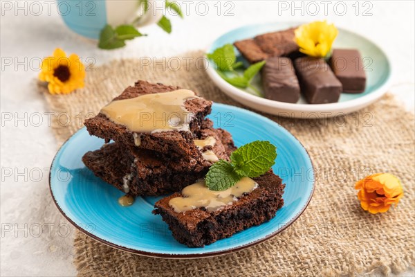 Chocolate brownie with caramel sauce with a cup of coffee on gray concrete background and linen textile. side view, close up