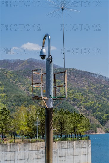 Round closed circuit camera on curved pole with lake and mountain under blue sky in background