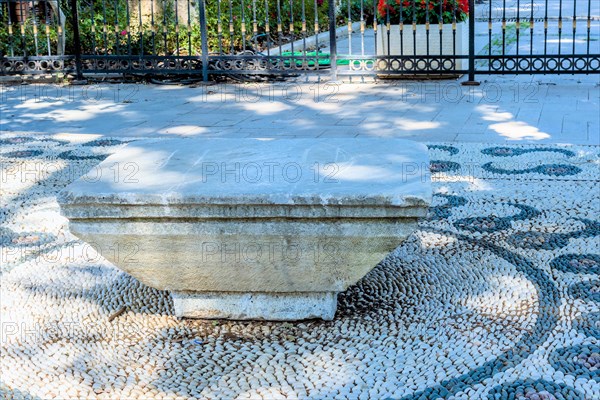 Concrete park bench on design of pebbles beside walkway under shade tree in Istanbul, Tuerkiye