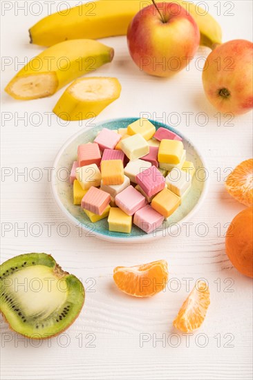 Various fruit jelly chewing candies on plate on white wooden background. apple, banana, tangerine, kiwi, side view, close up