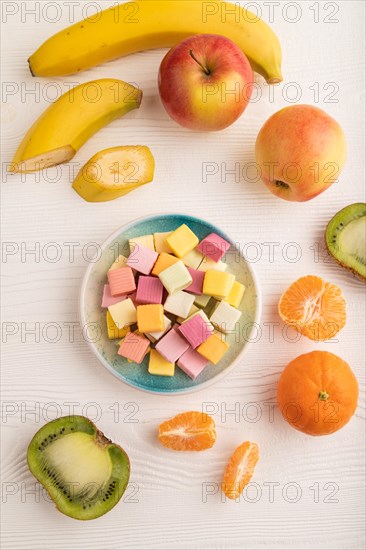 Various fruit jelly chewing candies on plate on white wooden background. apple, banana, tangerine, kiwi, top view, flat lay, close up