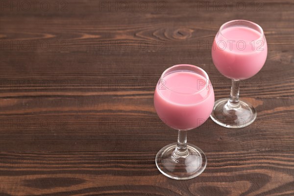 Sweet strawberry liqueur in glass on a brown wooden background. side view, copy space