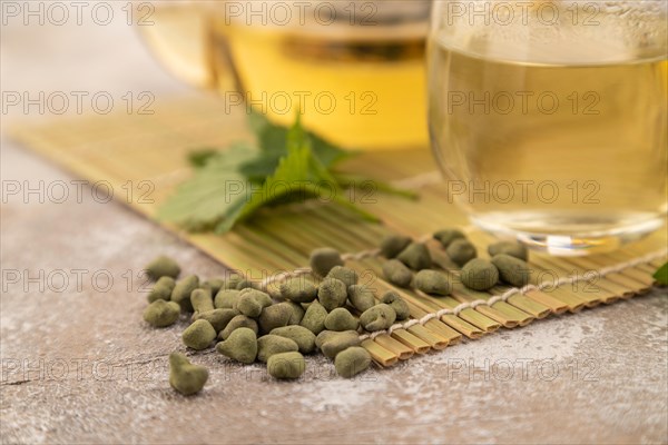 Green oolong tea with herbs in glass on brown concrete background. Healthy drink concept. Side view, close up, selective focus