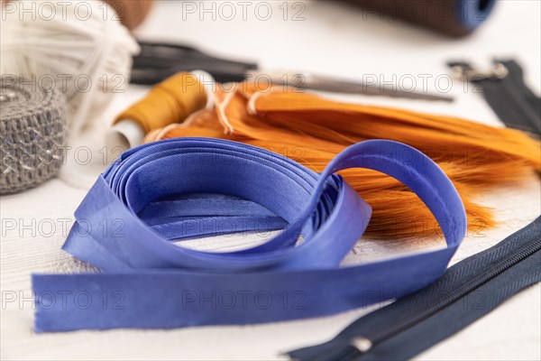 Sewing accessories: scissors, thread, thimbles, braid on white wooden background. Side view, close up, selective focus