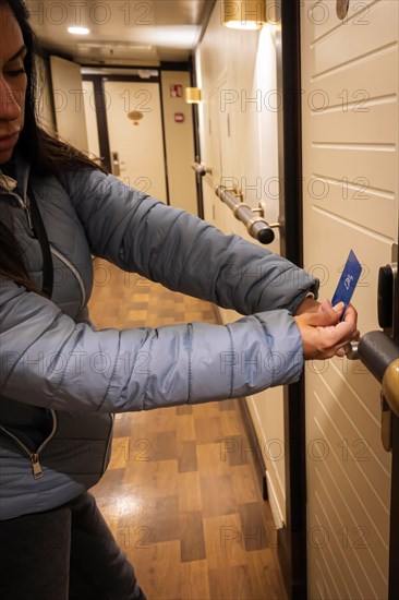 A latin woman in a corridor holding a key card to a door lock