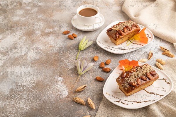 Caramel and almond cake with cup of coffee on brown concrete background and linen textile. side view, copy space