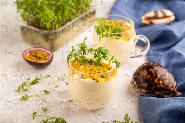 Yogurt with passionfruit and marigold microgreen in glass on gray concrete background with blue linen textile. Side view, close up, selective focus