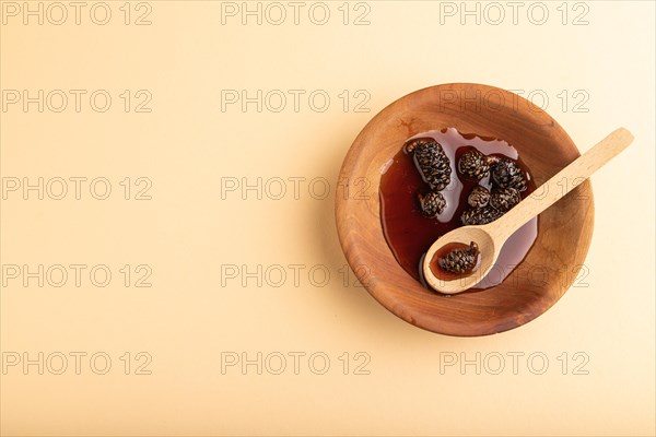 Pine cone jam in wooden bowl on orange pastel background. Top view, flat lay, copy space