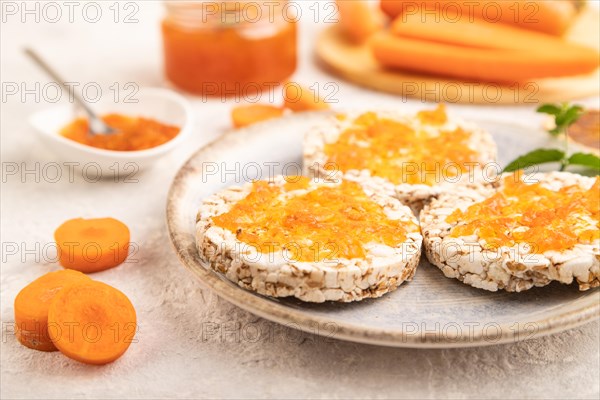 Carrot jam with puffed rice cakes on gray concrete background. Side view, close up, selective focus