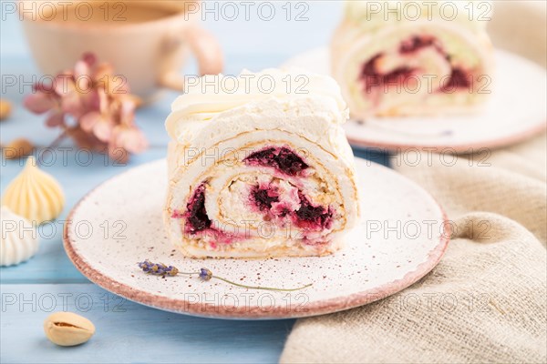 Roll biscuit cake with cream cheese and jam, cup of coffee on blue wooden background and linen textile. side view, close up, selective focus