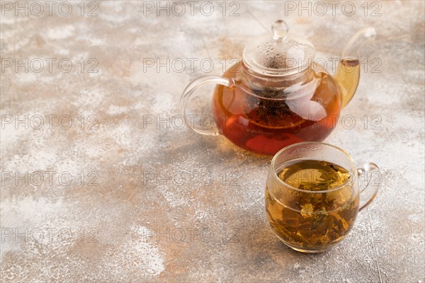 Red tea with herbs in glass teapot on brown concrete background. Healthy drink concept. Side view, copy space