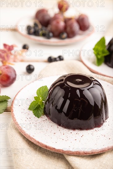 Black currant and grapes jelly on white wooden background and linen textile. side view, close up, selective focus