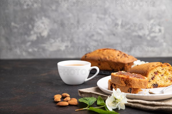 Homemade cake with raisins, almonds, soft caramel and a cup of coffee on a black concrete background and linen textile. Side view, copy space, selective focus