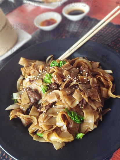 Vertical view of pad see ew or thai stir-fried noodles served in a black plate with chopsticks. Bangkok, Thailand, Asia