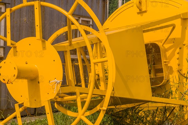 Bottom steel framework of ocean buoy laying in grass next to old rusty storage building in fishing village