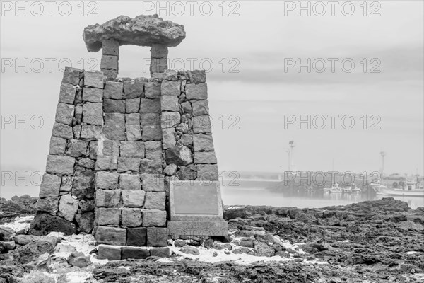 Black and white ancient lighthouse made of square cut stones on coast of small port on Jeju Island, South Korea, Asia