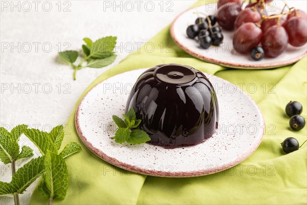 Black currant and grapes jelly on gray concrete background and green linen textile. side view, close up