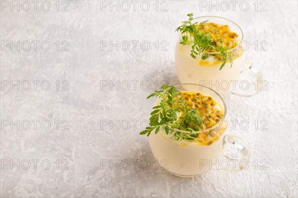 Yogurt with passionfruit and marigold microgreen in glass on gray concrete background. Side view, copy space