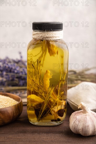 Sunflower oil in a glass jar with various herbs and spices, lavender, sesame, rosemary on a brown wooden background. Side view, close up