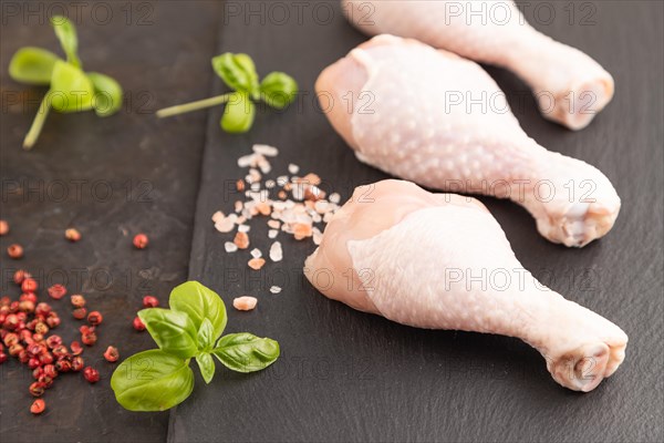 Raw chicken legs with herbs and spices on a black slate cutting board on a black concrete background and linen textile. Side view, close up, selective focus