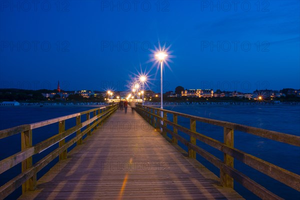 Nocturnal pier with illuminated street lamps and star effect, illuminated pier with strolling people and buildings, quiet, late evening mood, night on the beach with calm waves in deep twilight, clear, blue sky, star effect on the lanterns, motion blur, wipe effect, long exposure, view from the seaside to Ahlbeck, seaside resort, Usedom Island, Mecklenburg-Western Pomerania, Germany, Europe