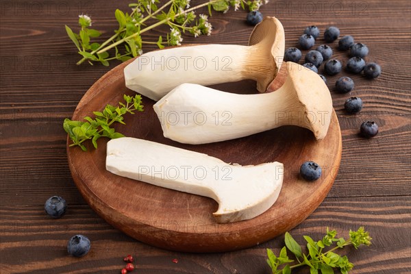 King Oyster mushrooms or Eringi (Pleurotus eryngii) on brown wooden background with blueberry, herbs and spices. Side view