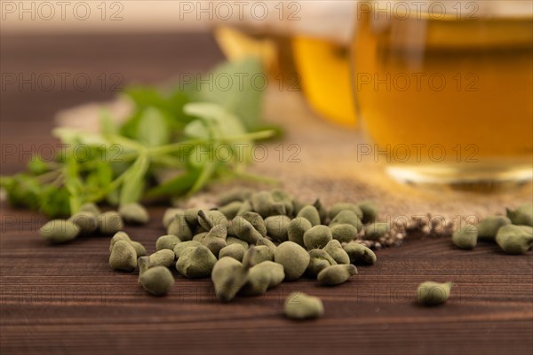 Green oolong tea with herbs in glass on brown wooden background and linen textile. Healthy drink concept. Side view, close up, selective focus