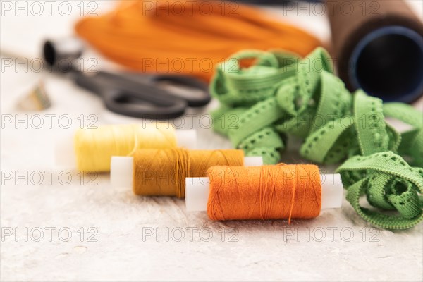 Sewing accessories: scissors, thread, thimbles, braid on gray concrete background. Side view, close up, selective focus