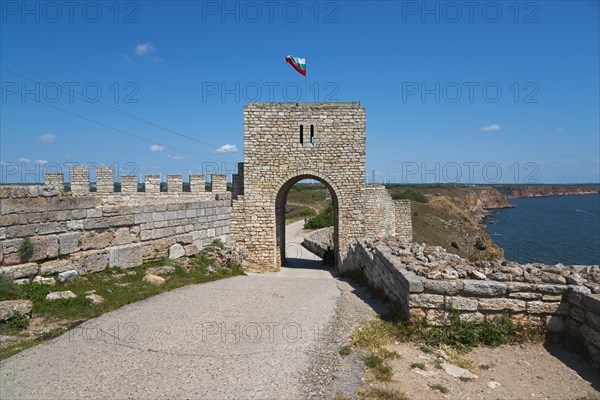 Stone fortress walls with arcade entrance and waving flag on a sunny day, fortress ruins, Cape Kaliakra, Dobruja, Black Sea, Bulgaria, Europe
